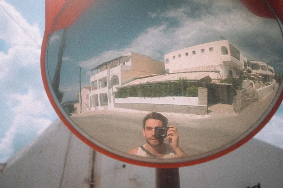 Self-portrait with a camera in a traffic mirror before white houses, analogue, flash by Kilian Amrehn