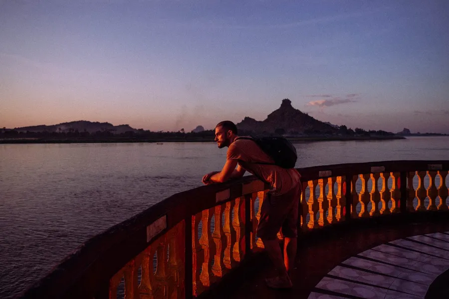 Man leans on a boat railing above a river in violet dusk, flash by Kilian Amrehn