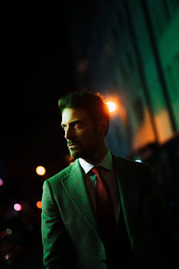 Man in a green jacket and tie lit by city lights at night, flash by Kilian Amrehn