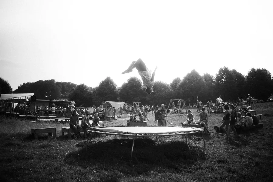 Person flips above a trampoline on a festival meadow, black and white, flash by Kilian Amrehn