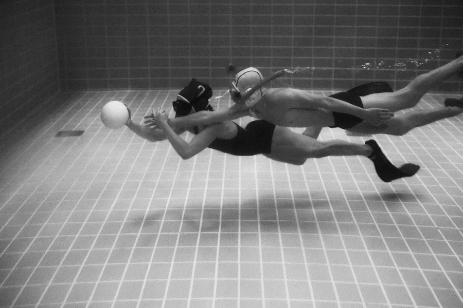 Two underwater rugby players dive for the ball in a pool, black and white, flash by Kilian Amrehn
