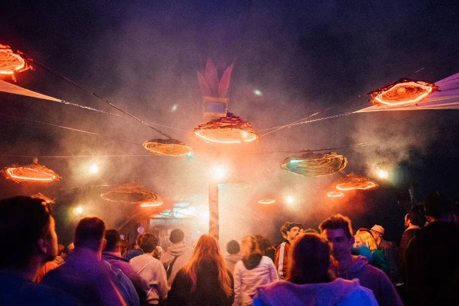 Festival stage with glowing lampshades above a crowd in haze at night, flash by Kilian Amrehn
