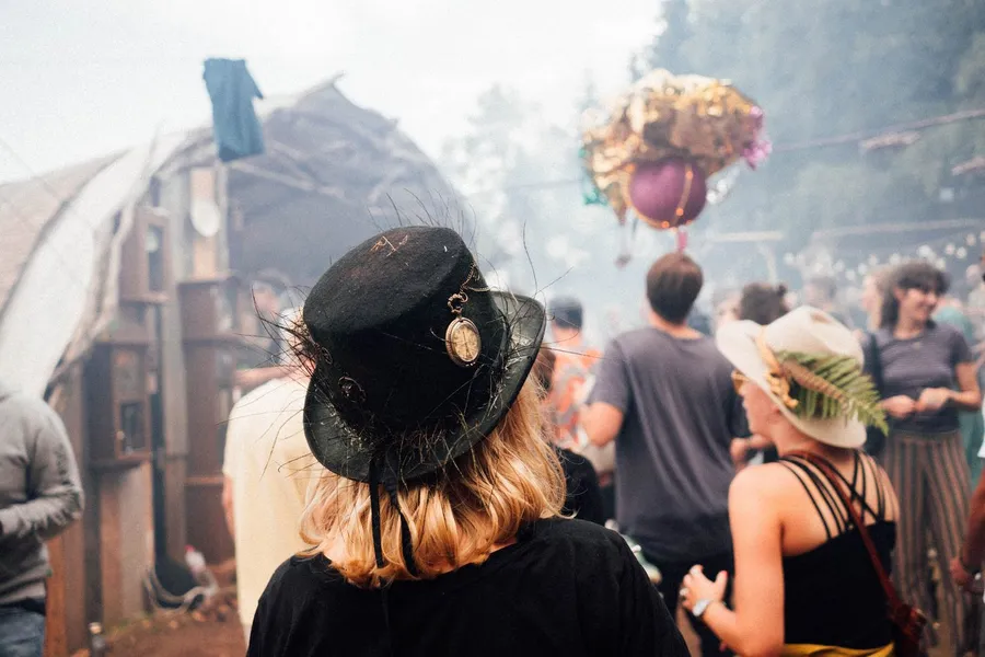 Woman in a top hat seen from behind in a hazy festival crowd with balloons, flash by Kilian Amrehn