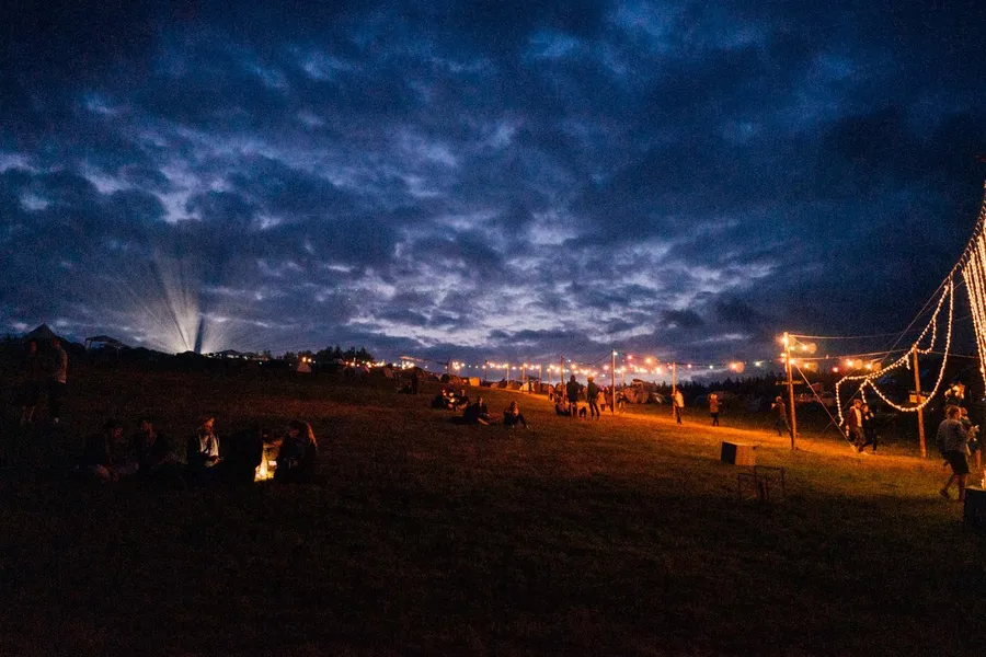 Festival meadow with string lights and campfires under a dark cloudy sky, flash by Kilian Amrehn