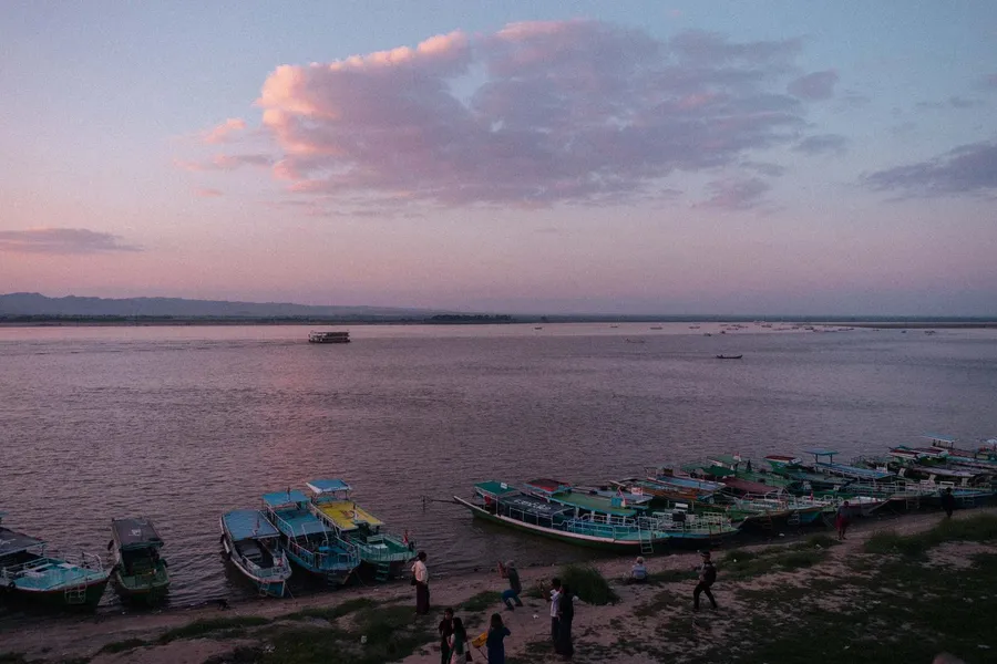 Colourful wooden boats on a riverbank at pink sunset, flash by Kilian Amrehn
