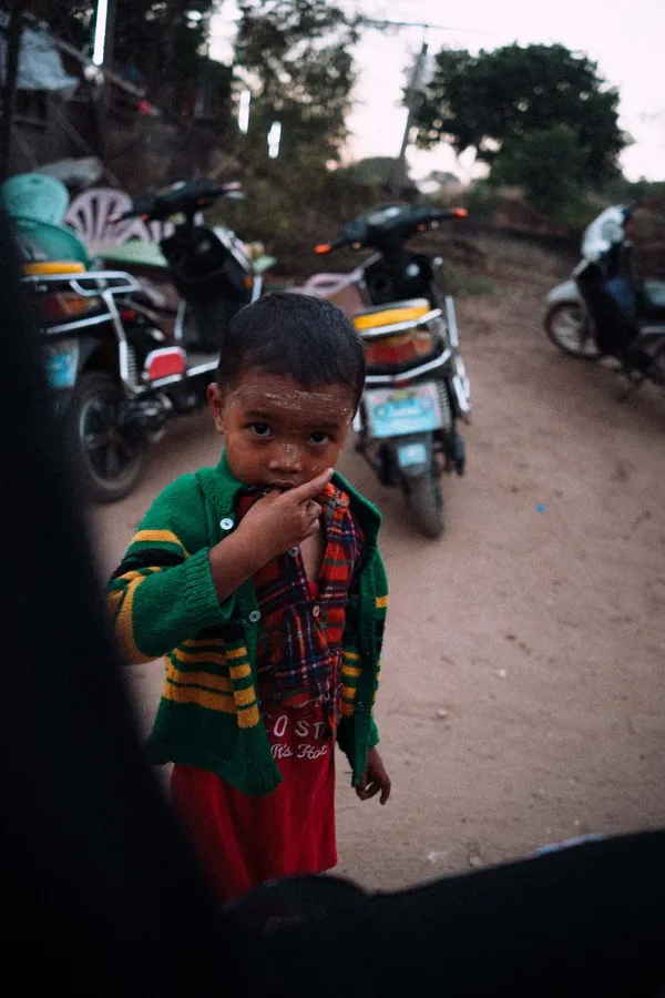 Small boy in a green cardigan among scooters on a dusty lane, flash by Kilian Amrehn