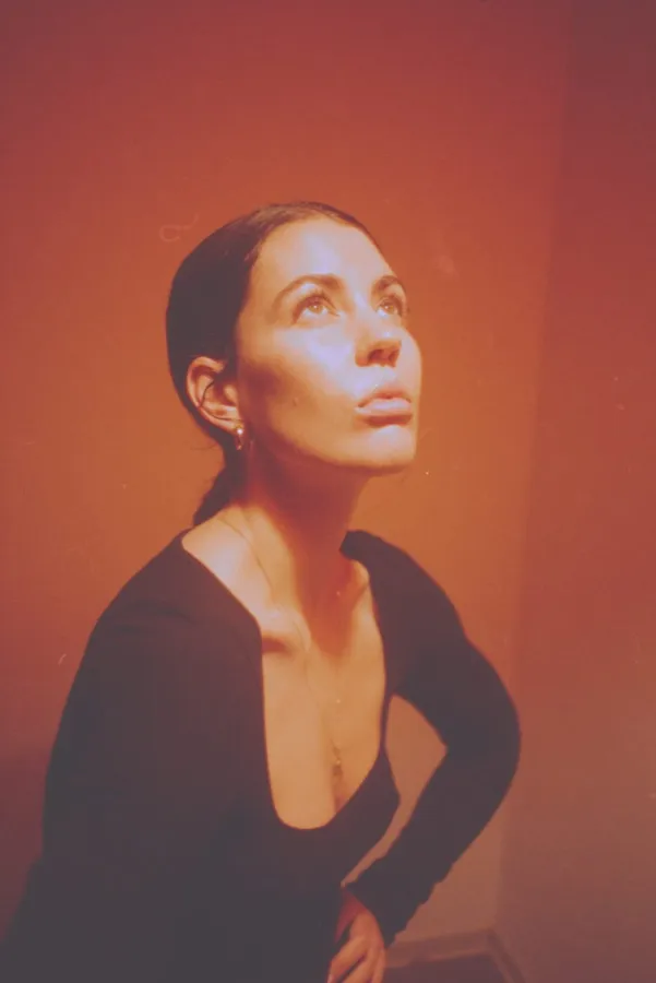 Woman with slicked-back hair looks upward in warm orange light, analogue, flash by Kilian Amrehn