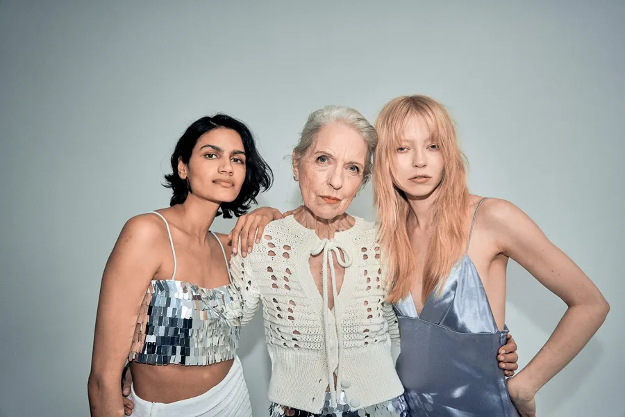 Three women of different generations arm in arm before a grey wall, flash by Kilian Amrehn