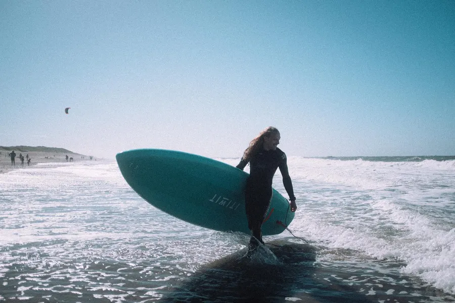 Surfer with her board walks out of the surf against the light, Denmark, flash by Kilian Amrehn