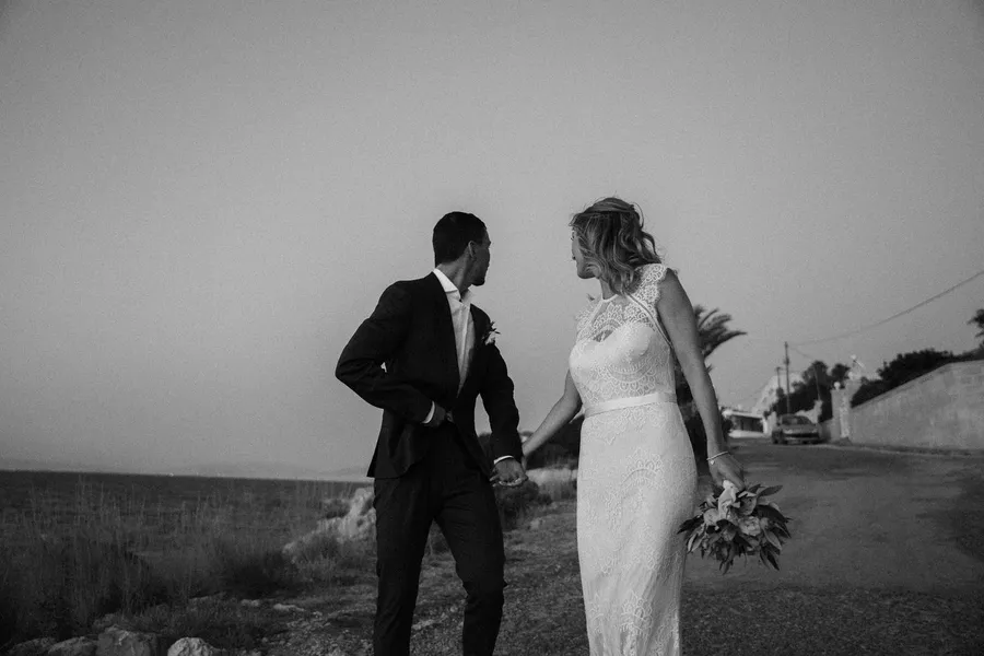 Bride and groom holding hands by the sea, black and white, Greece, flash by Kilian Amrehn