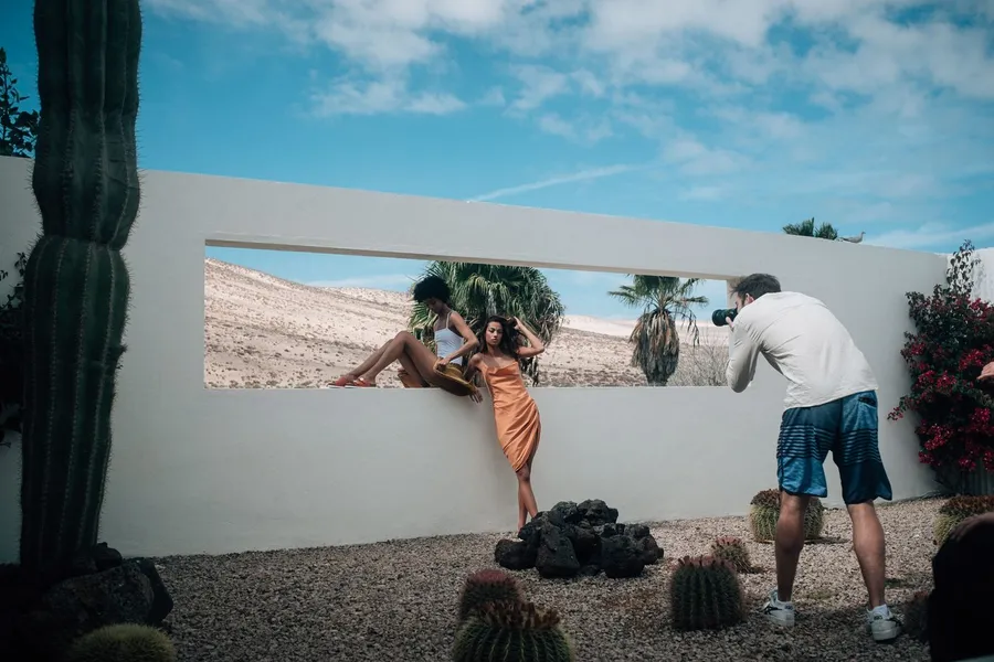 Photographer shoots two women at a white wall with a window opening and cacti, flash by Kilian Amrehn