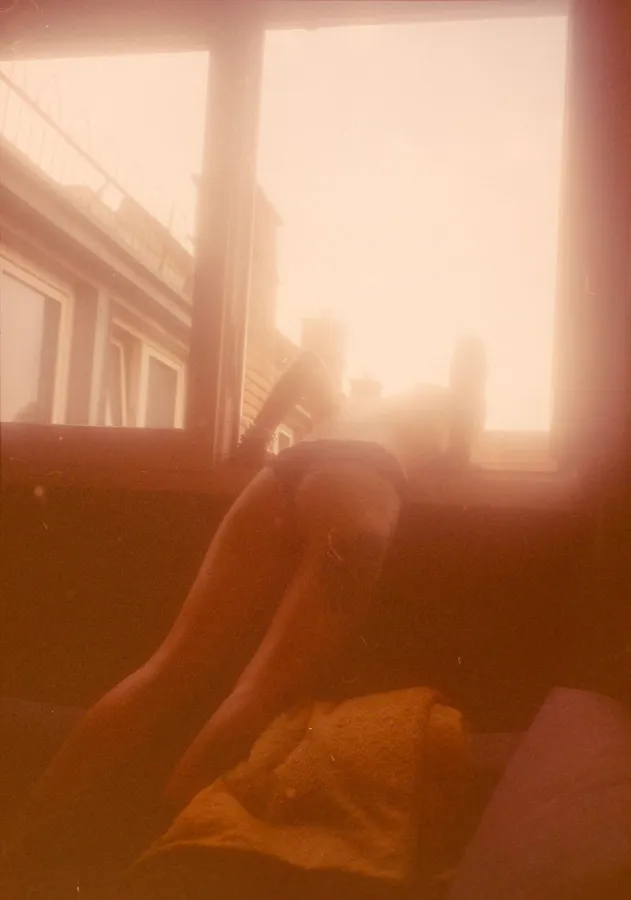 Legs on a sofa by a sunny window in overexposed red light, analogue, flash by Kilian Amrehn
