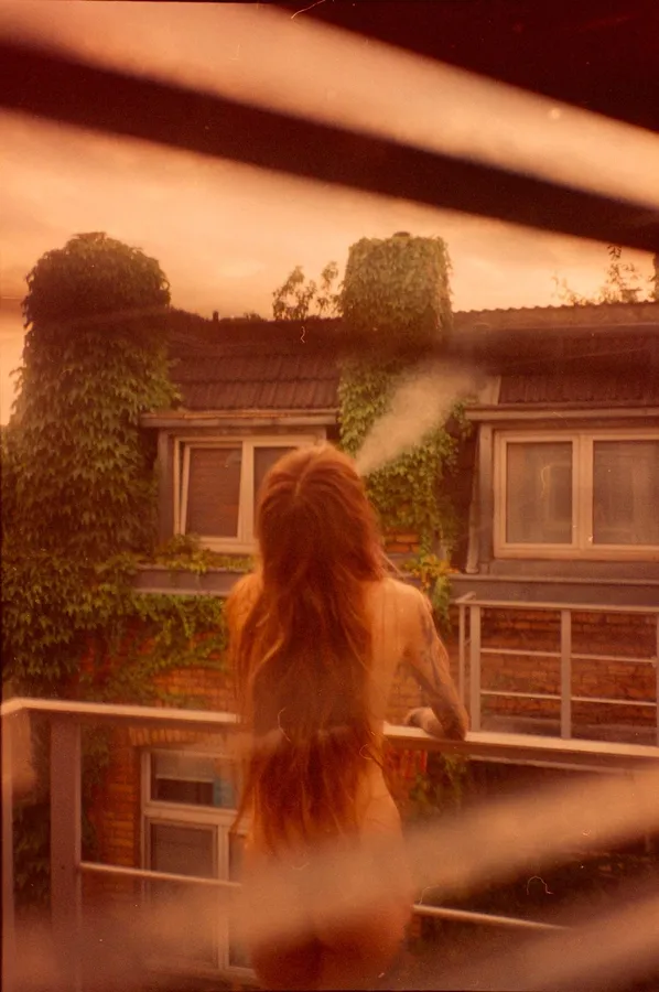 Woman with long red hair seen from behind on a balcony, warm light streaks, analogue, flash by Kilian Amrehn