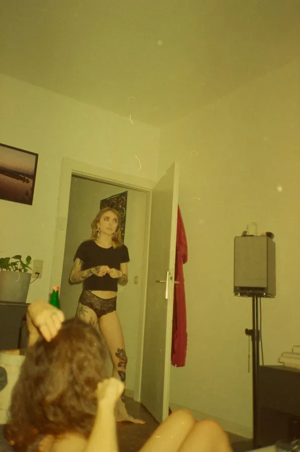 Woman in underwear stands in a doorway, a friend in the foreground, analogue, flash by Kilian Amrehn