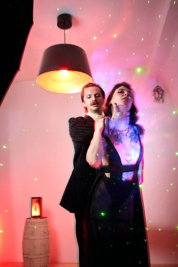 Couple posing under a pendant lamp, green laser dots on a pink wall, flash by Kilian Amrehn