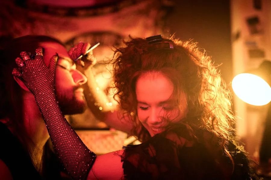 Man with a fishnet glove and a curly-haired woman laughing in the warm backlight of a lamp, flash by Kilian Amrehn