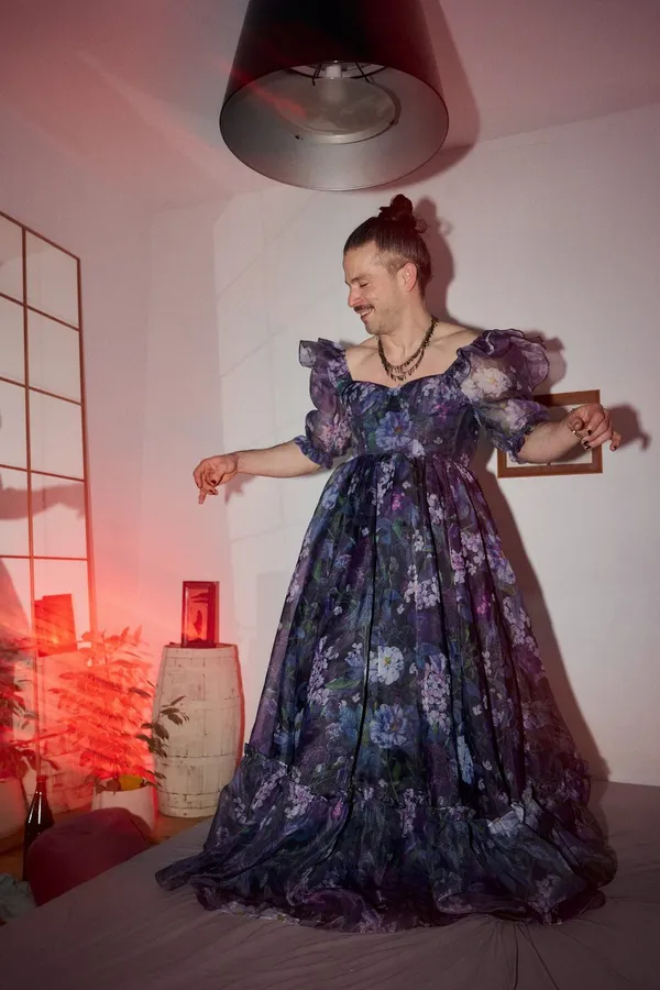 Man in a floor-length floral ball gown dancing in a bedroom, red light and pendant lamp, flash by Kilian Amrehn