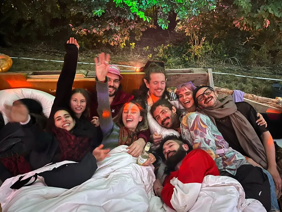 Group of friends lying laughing under blankets beneath trees, at night with flash, flash by Kilian Amrehn