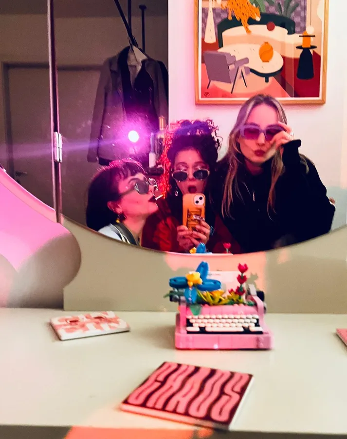 Mirror selfie of three women in sunglasses, flash, pink typewriter on the table, flash by Kilian Amrehn