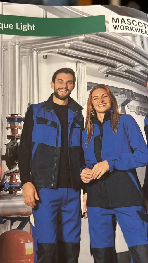 Man and woman in blue workwear smiling at a trade fair booth, flash by Kilian Amrehn