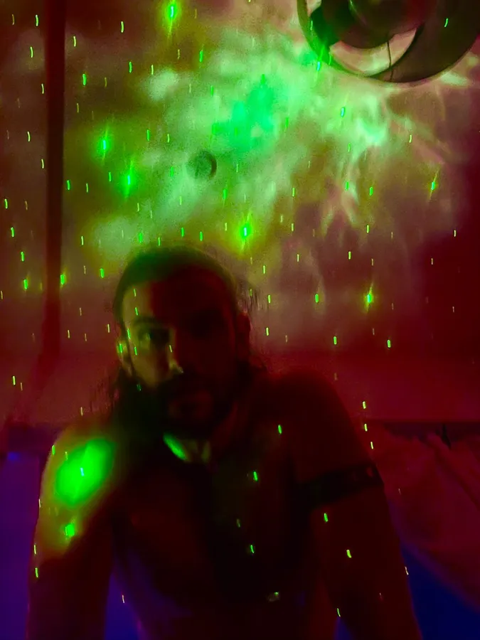 Man in the dark under green laser dots and a nebula projection, red light, flash by Kilian Amrehn