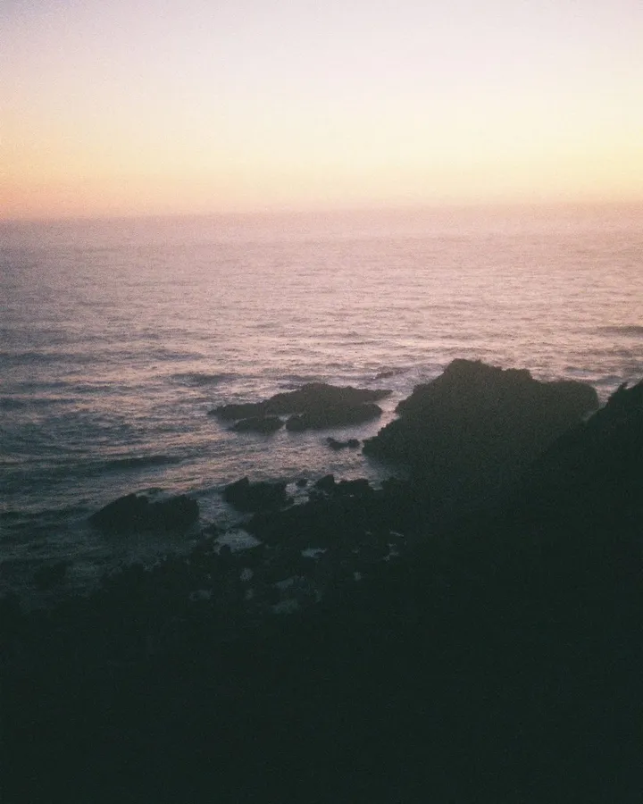 Analogue: sunset over the sea, dark rocks in the foreground, pastel sky, flash by Kilian Amrehn