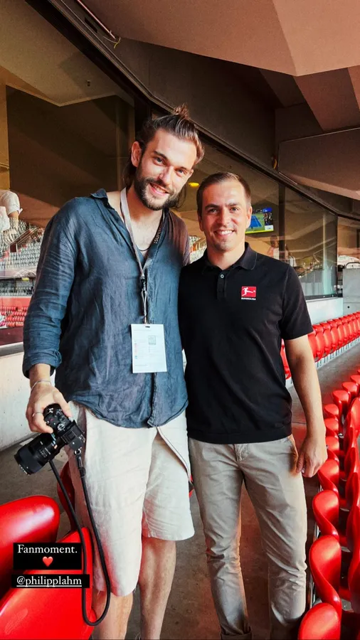 Photographer with camera and lanyard next to a man among red stadium seats, flash by Kilian Amrehn