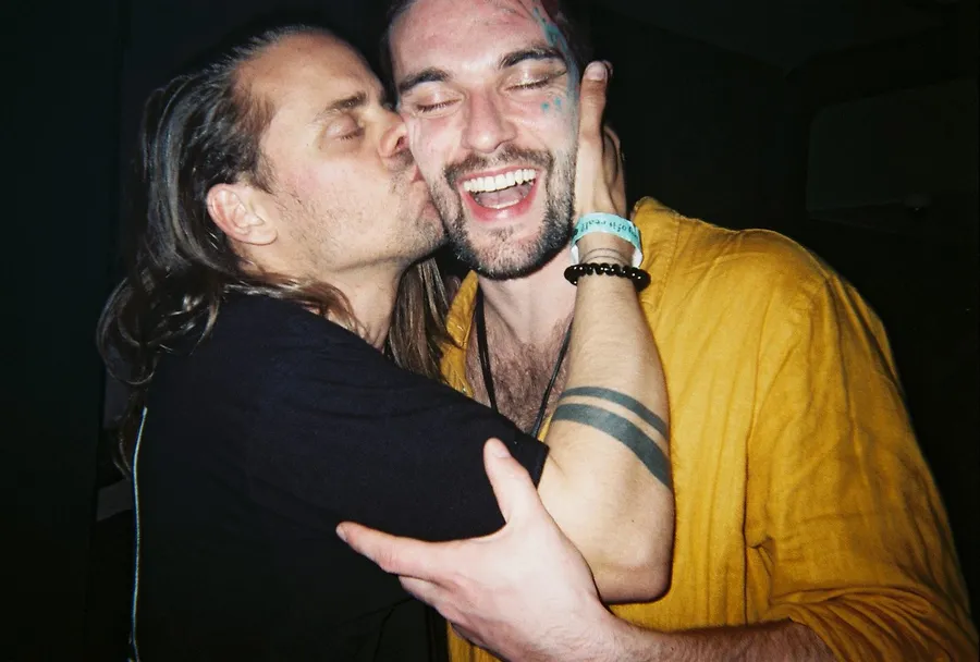 Analogue flash: man kissing a laughing friend in a yellow shirt on the cheek, flash by Kilian Amrehn