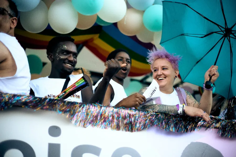 Pride parade: laughing people on a float with balloons, rainbow flag and umbrella, flash by Kilian Amrehn