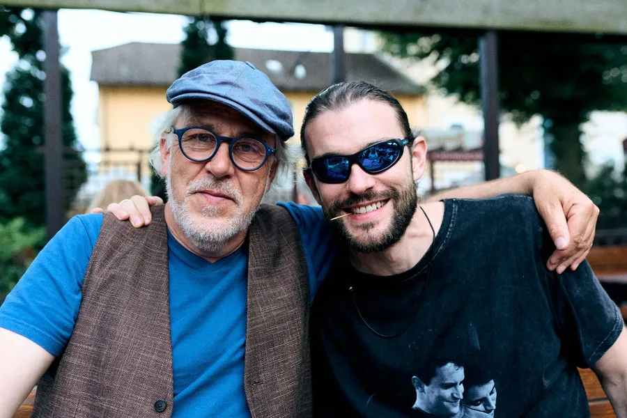 Older man in a flat cap and a laughing friend in sport sunglasses in a beer garden, flash by Kilian Amrehn