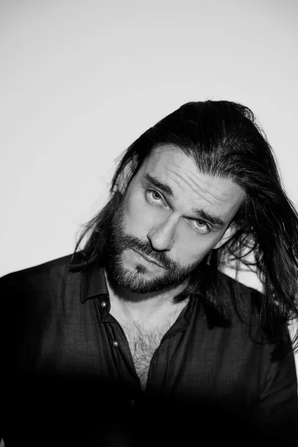 Black and white portrait of a man with long hair and beard, looking into the camera, flash by Kilian Amrehn