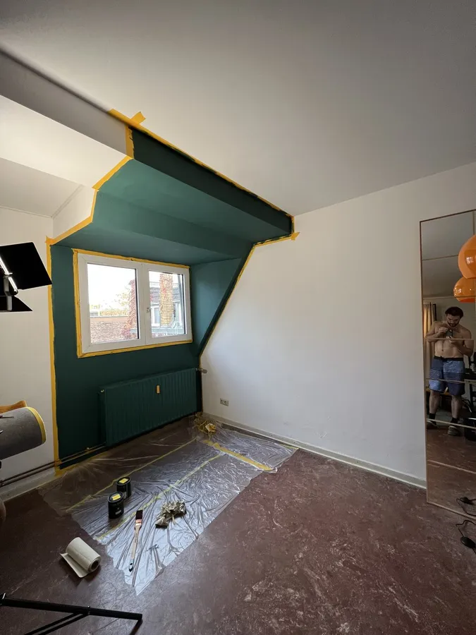 Empty room with a sloped ceiling and a freshly painted dark green wall, drop sheet on the floor, flash by Kilian Amrehn