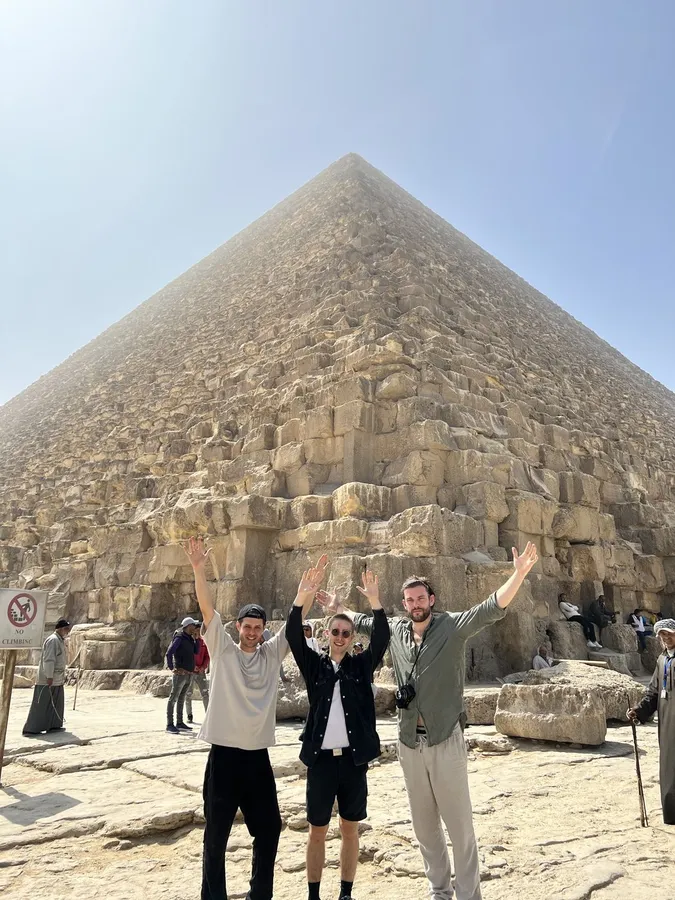 Three friends throwing their arms up in front of the Great Pyramid, Giza, flash by Kilian Amrehn