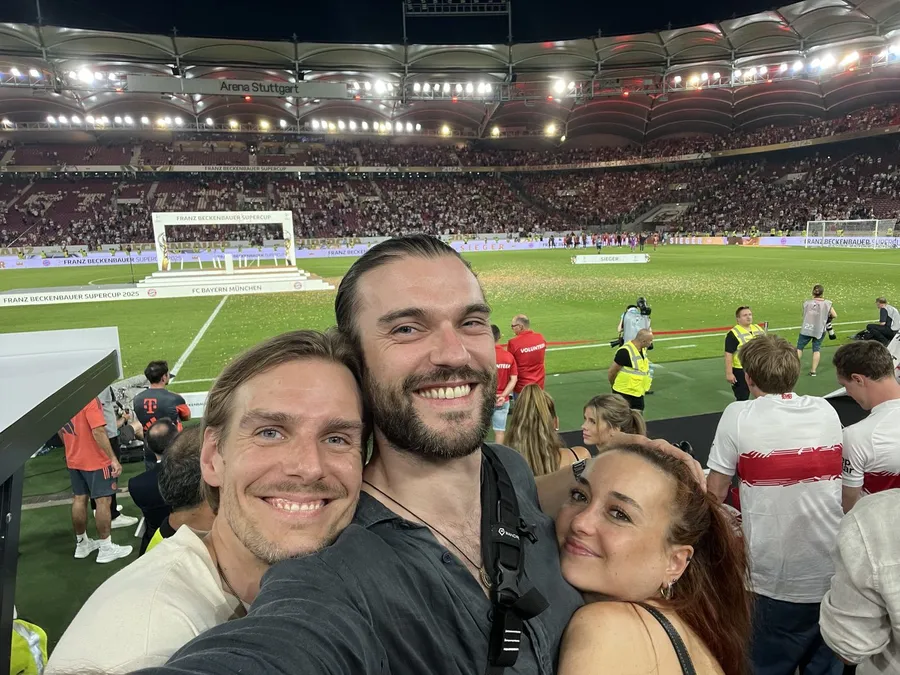 Selfie of three friends in a football stadium under floodlights, pitch covered in confetti, flash by Kilian Amrehn