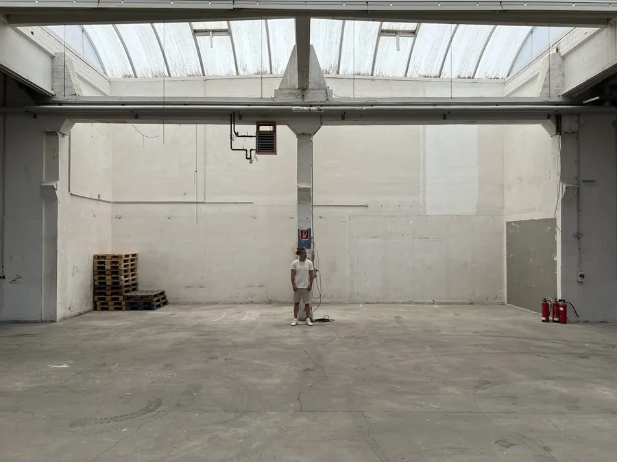 Man standing small in a huge empty hall with skylights and a concrete floor, flash by Kilian Amrehn