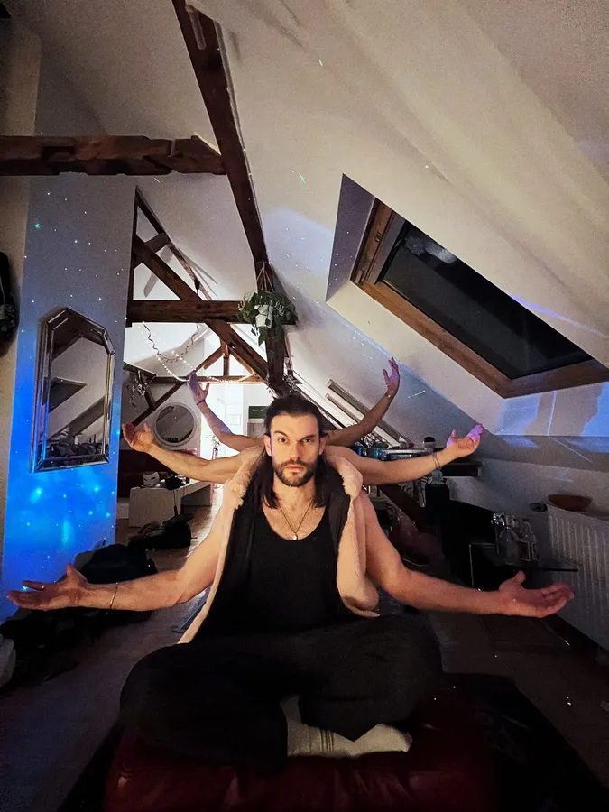 Man sitting cross-legged under roof beams, four arms behind him like a deity, flash by Kilian Amrehn