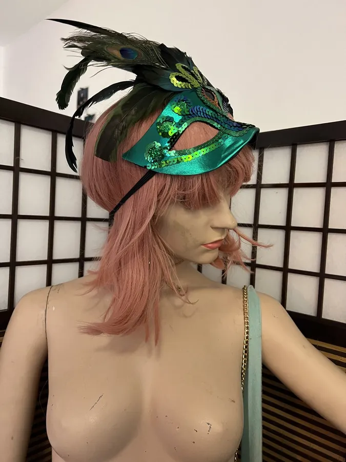 Mannequin with a pink wig and green feathered mask in front of a folding screen, flash by Kilian Amrehn