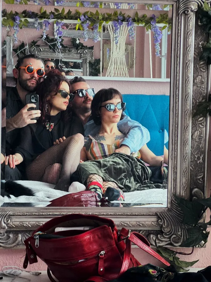 Friends in sunglasses on a bed, seen in an ornate silver mirror, flash by Kilian Amrehn