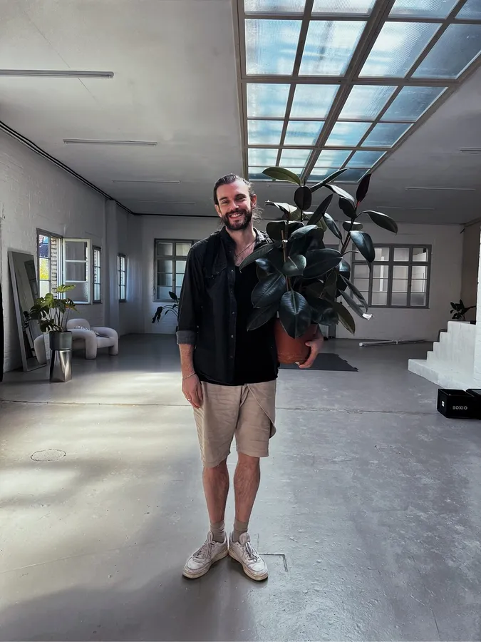 Man holding a large houseplant in a bright loft with a glass roof, flash by Kilian Amrehn
