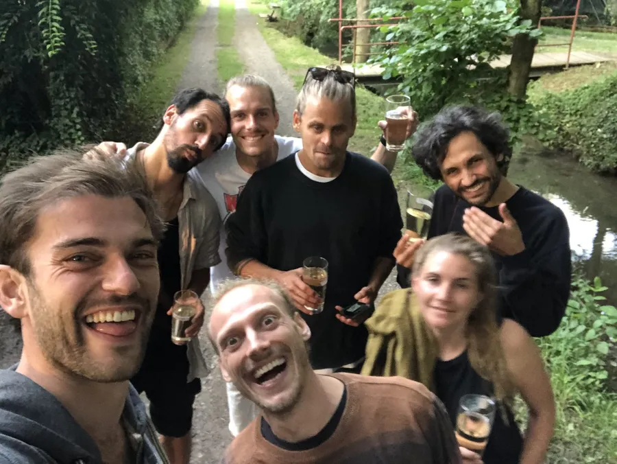 Group of friends with glasses of sparkling wine taking a selfie on a green creek path, flash by Kilian Amrehn