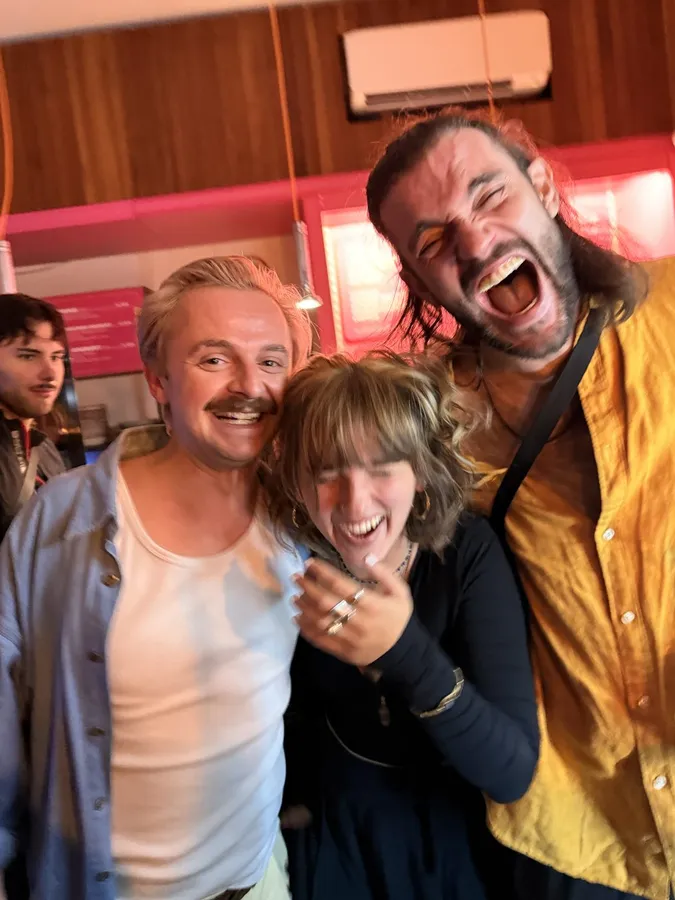Three friends pulling faces and laughing in a pink kitchen, flash by Kilian Amrehn