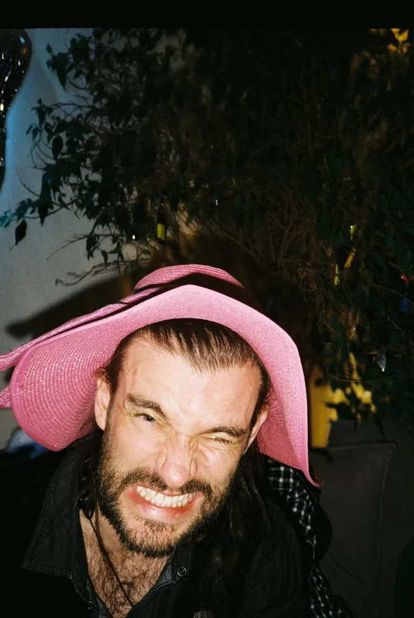 Man in a pink hat squinting with a grin, at night with flash, flash by Kilian Amrehn