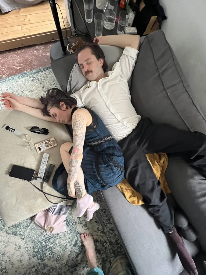 Two people asleep, exhausted, on a sofa and rug, phones and glasses scattered around, flash by Kilian Amrehn