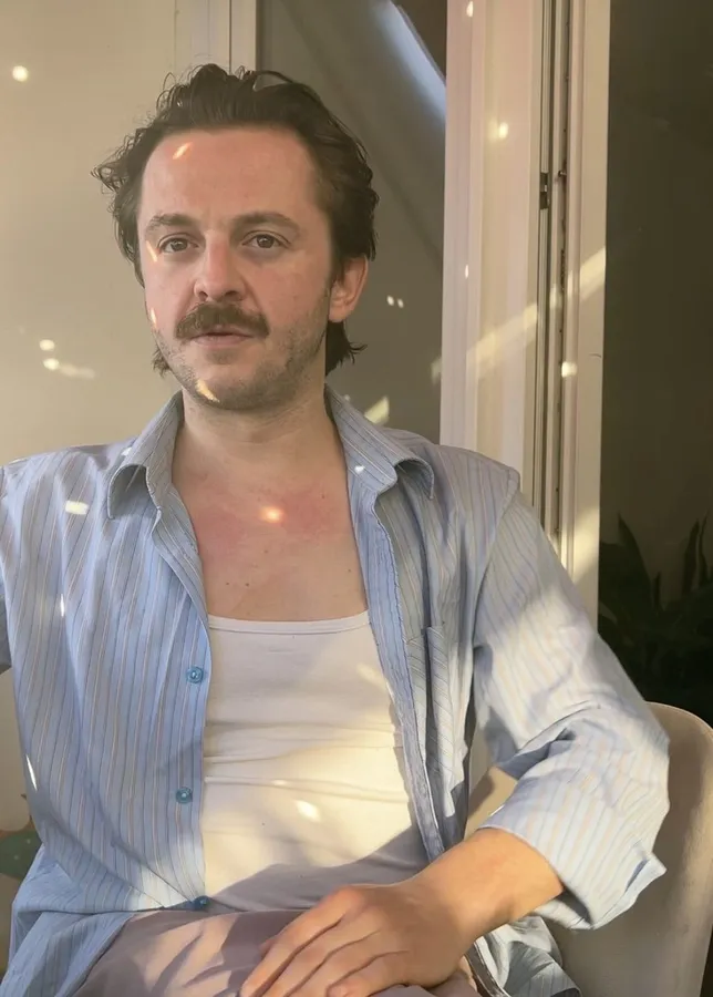 Man with a moustache and open shirt in warm window light, flash by Kilian Amrehn