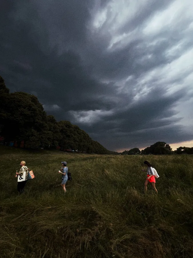 Three people walking through tall grass under dark storm clouds, flash by Kilian Amrehn