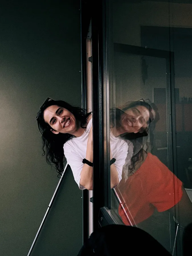 Woman leaning out of a glass door laughing, her reflection in the glass, flash by Kilian Amrehn