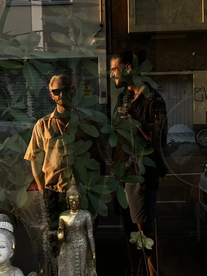 Two men reflected in a shop window with Buddha figures and plants, flash by Kilian Amrehn