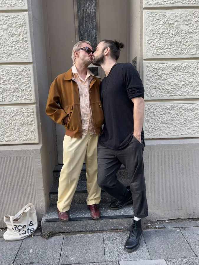 Two men kissing in a doorway, suede jacket and black outfit, flash by Kilian Amrehn