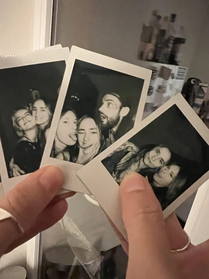 Hands holding black and white instant photos of laughing friends, flash by Kilian Amrehn