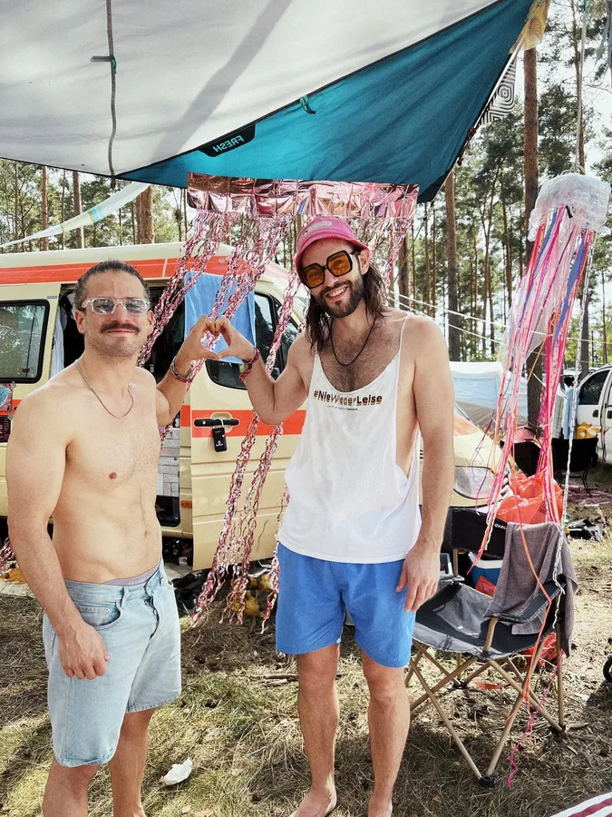 Two men at a festival campsite, van with tinsel and tarp roof, flash by Kilian Amrehn